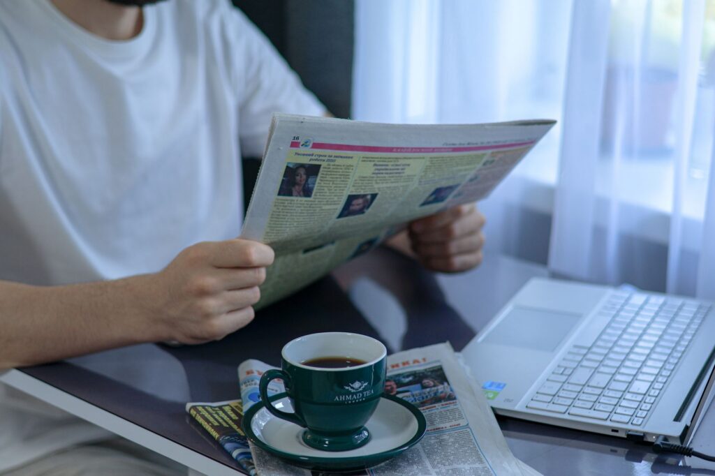 Ziar economic deschis lângă o ceașcă de cafea și un laptop, pe biroul unui antreprenor